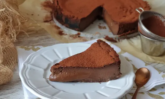 Un trozo de pastel de chocolate cubierto de cacao en polvo, con el pastel entero al fondo.
