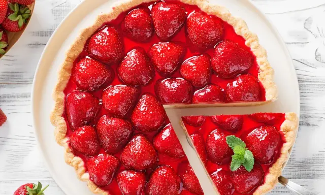 Deliciosa tarta de fresas cubierta con gelatina brillante y fresas frescas. Una porción se ha cortado, revelando la jugosa fruta.