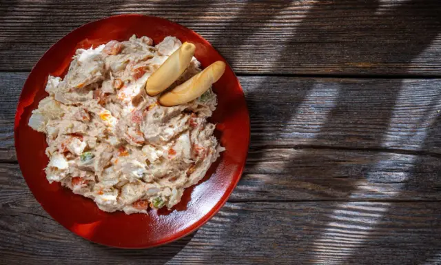 Ensaladilla rusa cremosa en plato rojo, con palitos de pan. ¿Cuanto dura la ensaladilla rusa en la nevera?