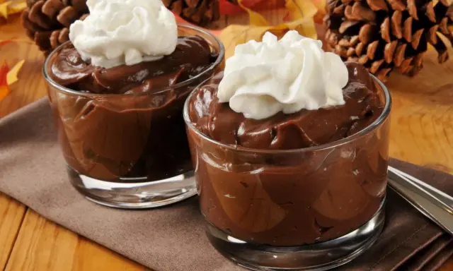 Dos copas de cremosas natillas de chocolate con nata montada, decoradas con piñas y hojas de otoño.