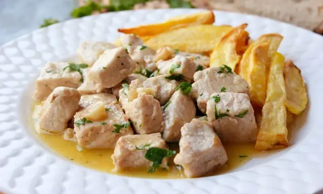 Sabroso lomo al ajillo en trozos, bañado en aceite y ajo, acompañado de patatas fritas crujientes.