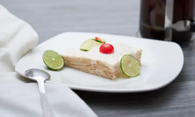 Deliciosa carlota de limón, con galletas y crema, decorada con rodajas de lima y una cereza.