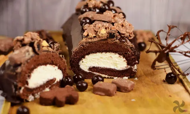 Delicioso rollo de chocolate cubierto con crema y decorado con más chocolate y dulces.