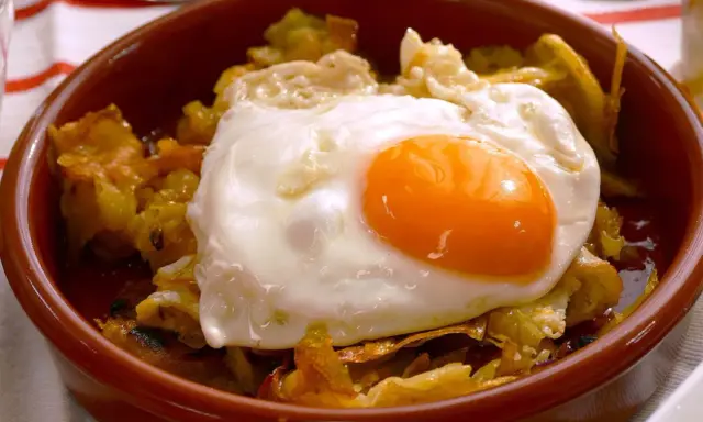 Un plato de patatas fritas con pimientos y un huevo estrellado encima, listo para disfrutar.