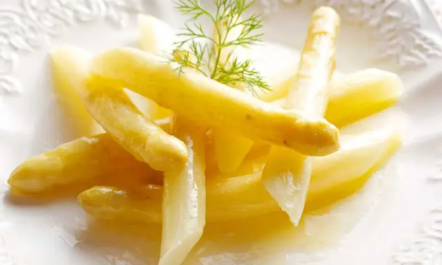 Espárragos blancos tiernos, listos para cocinar, servidos en un plato blanco con una ramita de eneldo.