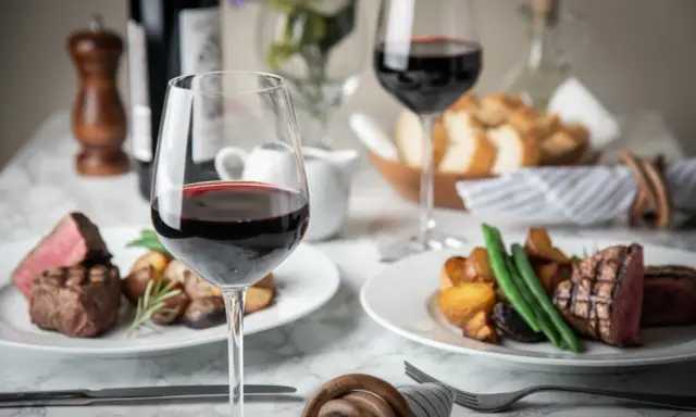 Dos copas de vino tinto, filetes jugosos y patatas asadas, perfectos para una cena de vino de invierno.