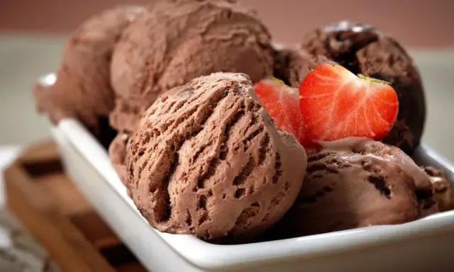 Cucharadas de cremoso helado de chocolate, decoradas con fresas frescas, listas para disfrutar.