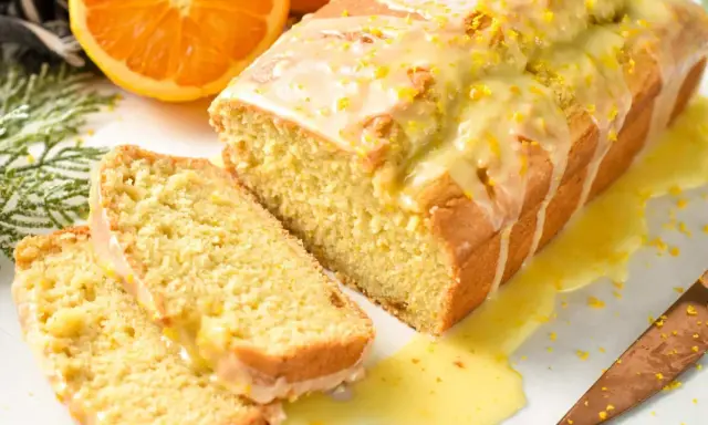 Un delicioso bizcocho de naranja, cubierto con glaseado y ralladura, con dos rebanadas cortadas.