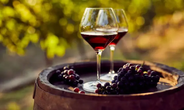 Dos copas de vino tinto y racimos de uvas sobre un barril de madera, evocando las mejores añadas de Ribera del Duero.