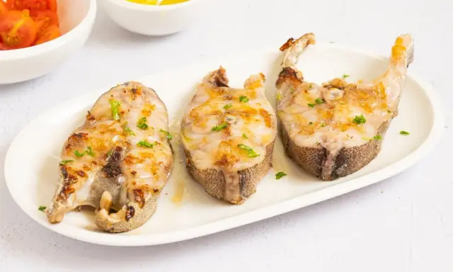 Tres rodajas de mero a la plancha, doradas y con perejil picado, servidas en plato blanco.