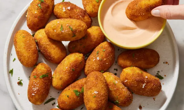 Croquetas de patata doradas y crujientes, espolvoreadas con perejil y sal, listas para ser mojadas en una cremosa salsa rosa.