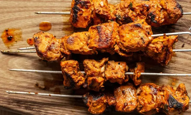 Cuatro brochetas de pinchos morunos auténticos, jugosos y dorados, sobre una tabla de madera.