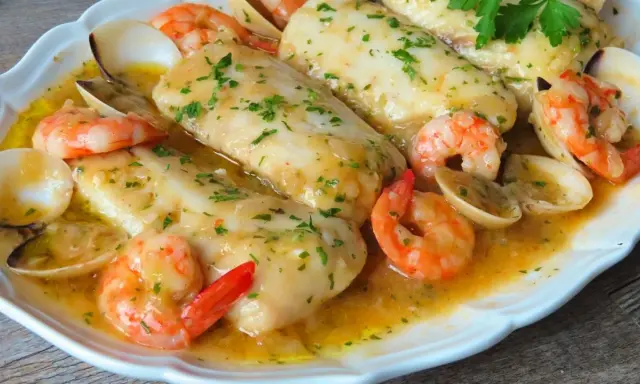 Merluza a la marinera con gambas y almejas, un plato delicioso bañado en salsa.