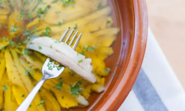 Boquerones en vinagre, la receta de la abuela, listos para disfrutar. Un tenedor recoge un boquerón marinado en aceite y vinagre, espolvoreado con perejil.