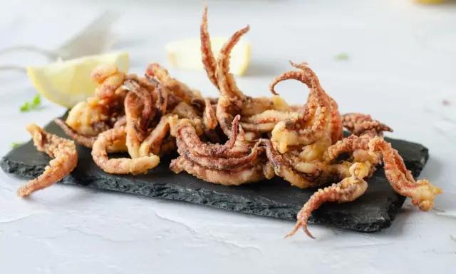 Crujientes rejos fritos servidos sobre pizarra negra, acompañados de gajos de limón.