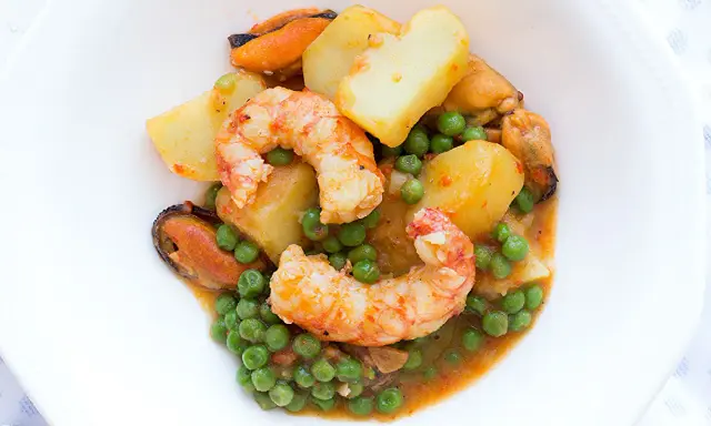 Patatas a la marinera con gambas, mejillones y guisantes en una salsa sabrosa.