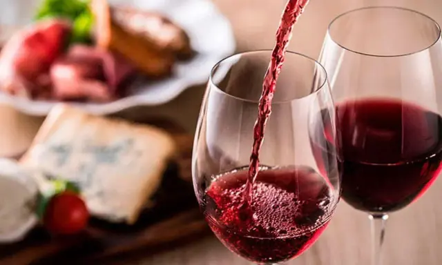 Vino tinto servido en copas, con tabla de quesos y embutidos al fondo. Una cata para apreciar la diferencia entre tempranillo y crianza.