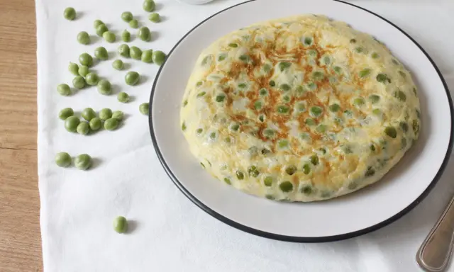 Tortilla de guisantes recién hecha, dorada y esponjosa, con guisantes verdes esparcidos por encima.