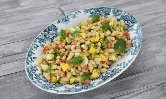 Deliciosa ensalada de alubias con trozos de tomate, mango y huevo, decorada con hojas de menta fresca.