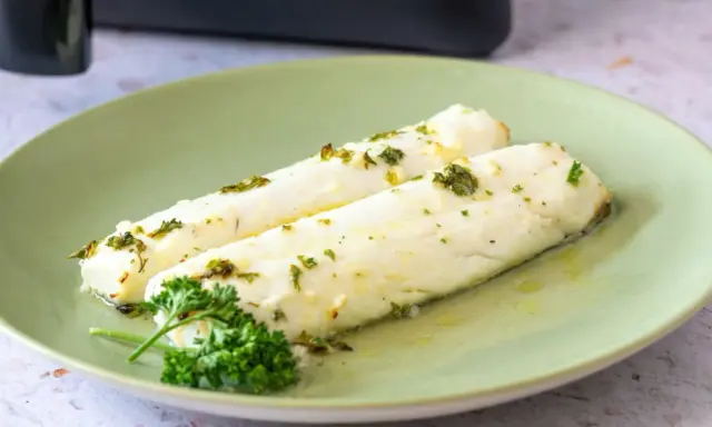Dos filetes de merluza jugosos, recién salidos de la airfryer, con hierbas frescas y aceite de oliva.