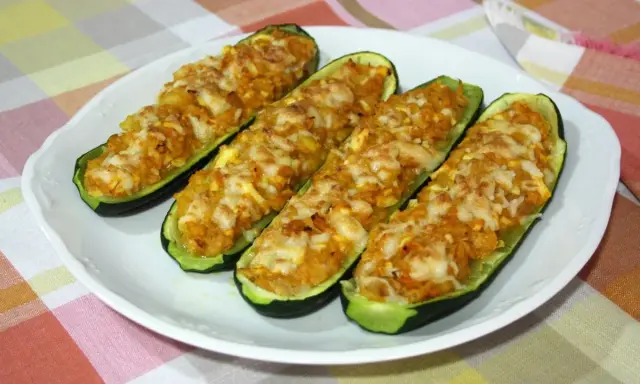 Cuatro calabacines rellenos de atún, gratinados con queso, servidos en un plato blanco sobre un mantel a cuadros.