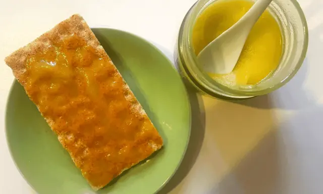 Galleta con mermelada de aceite de oliva, servida en plato verde junto a un tarro con la mermelada y una cuchara.