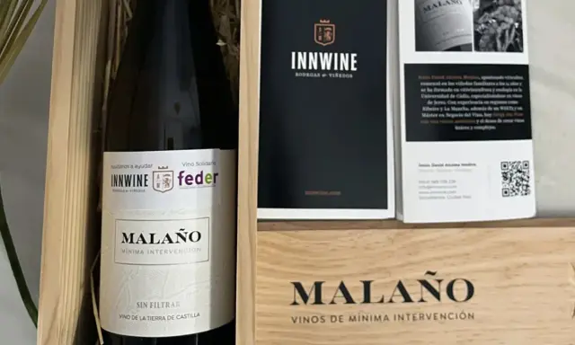 Caja de vino "Malaño" con etiqueta "Vino Solidario" y logos de INNWINE y feder. Incluye folleto informativo.