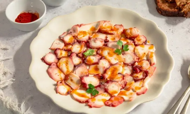 Delicioso carpaccio de pulpo, finas láminas con pimentón y perejil, servido en plato blanco.