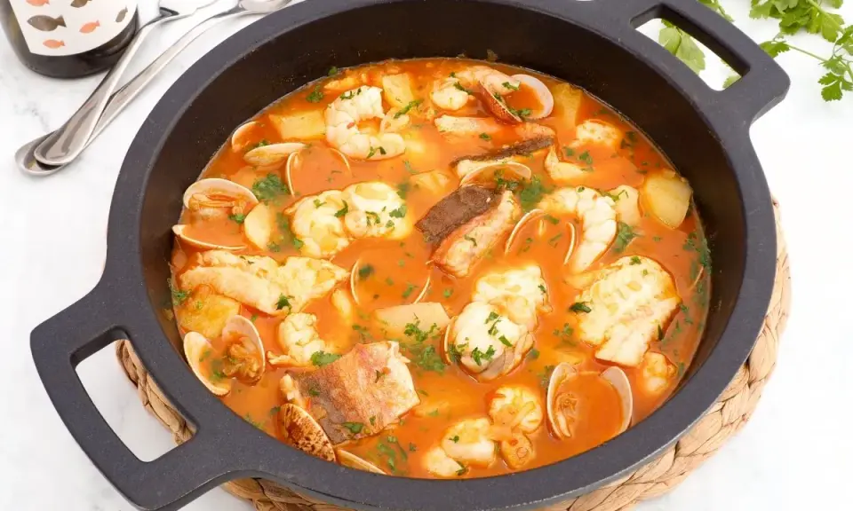 Una deliciosa cazuela de pescado con gambas, almejas y trozos de pescado blanco en una rica salsa roja, adornada con perejil fresco.