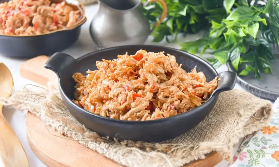 Delicioso pollo mechado con pimientos rojos y cebolla, servido en un cuenco negro sobre arpillera.