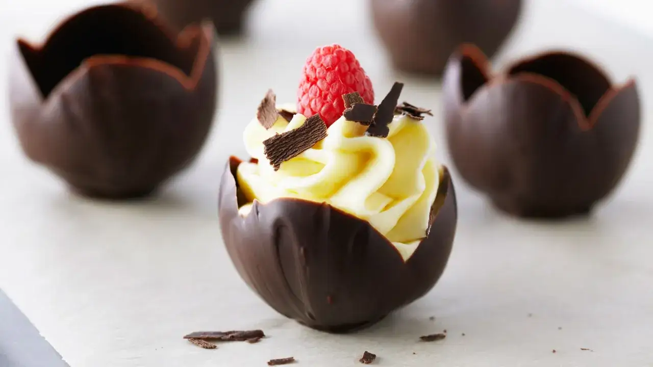 Deliciosas natillas de chocolate, cremosas y cubiertas con virutas de chocolate y una frambuesa fresca.