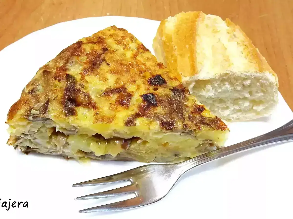 Una porción de tortilla de champiñones con patatas, acompañada de pan y un tenedor.