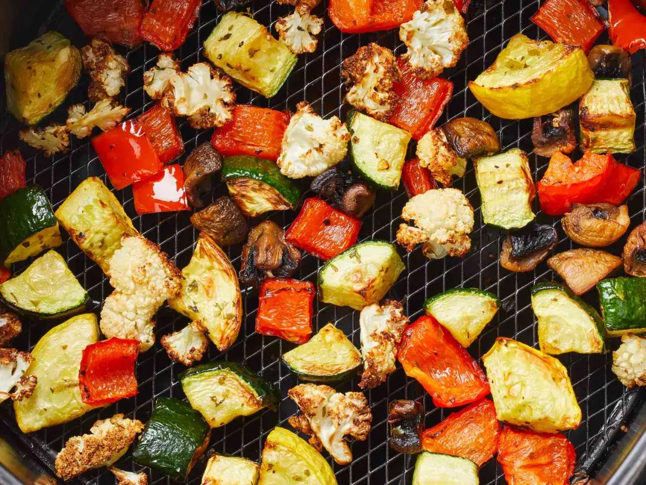 Verduras airfryer: pimientos rojos, calabac&iacute;n, coliflor y champi&ntilde;ones asados en una rejilla.