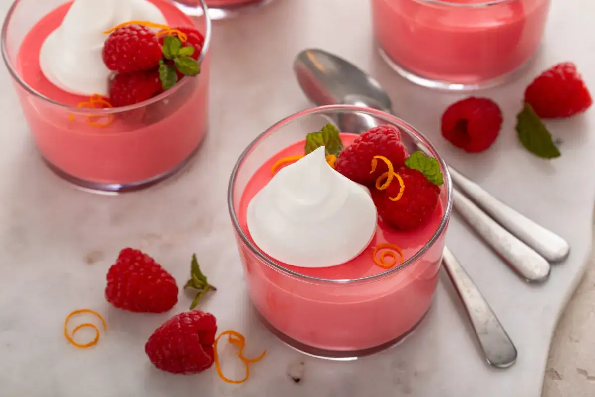 Delicioso mousse de yogur de frambuesa con crema batida, frambuesas frescas y ralladura de naranja.