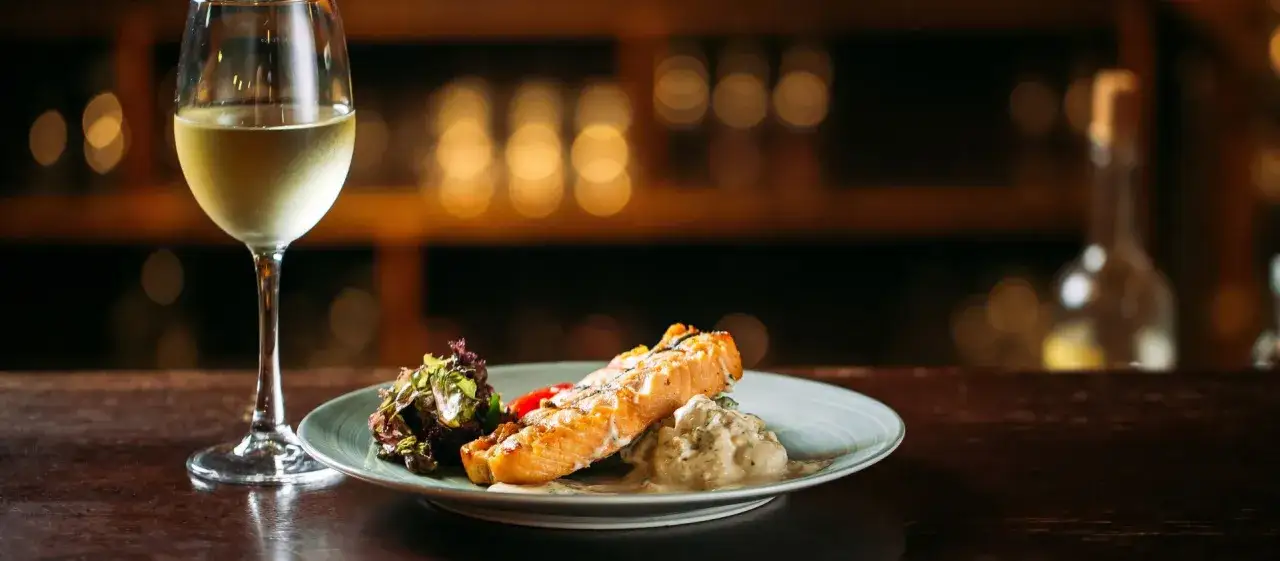 Un plato de salm&oacute;n a la parrilla con ensalada y una copa de vino blanco, perfecto para un maridaje con riesling.