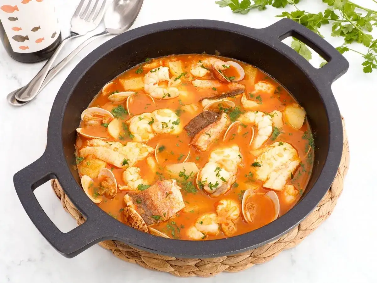 Una deliciosa cazuela de pescado con gambas, almejas y trozos de pescado blanco en una rica salsa de tomate, adornada con perejil fresco.