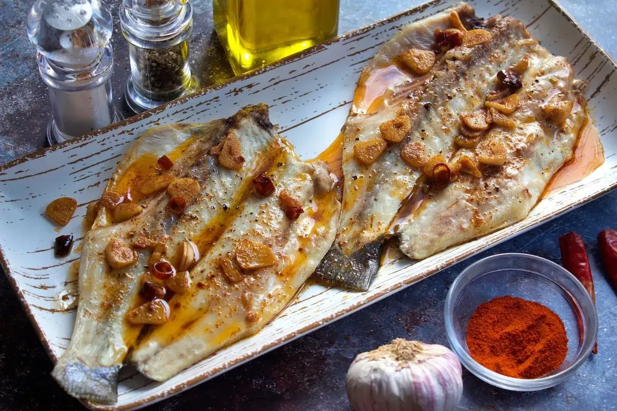 Dos filetes de lubina a la bilbaina, dorados y jugosos, con l&aacute;minas de ajo y guindilla.