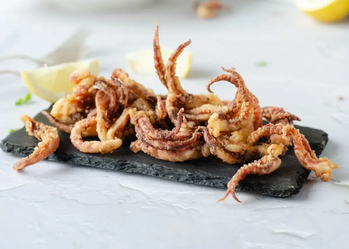 Crujientes rejos fritos servidos en una pizarra negra, acompa&ntilde;ados de gajos de lim&oacute;n.