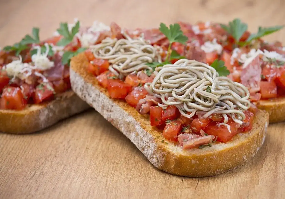 Tostadas con tomate picado, jamón y una generosa porción de ensalada de gulas, adornadas con perejil fresco.