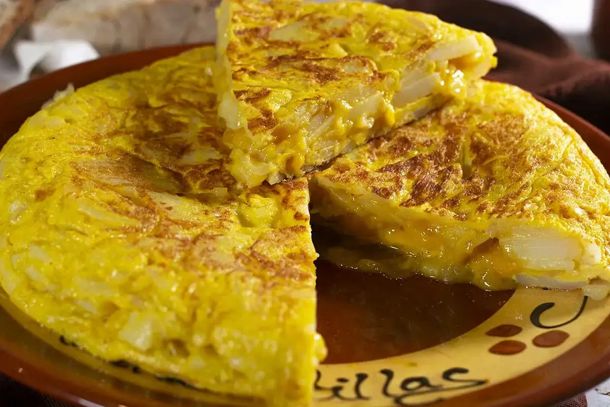 Una jugosa tortilla de patatas, dorada por fuera y tierna por dentro, servida en un plato de barro.