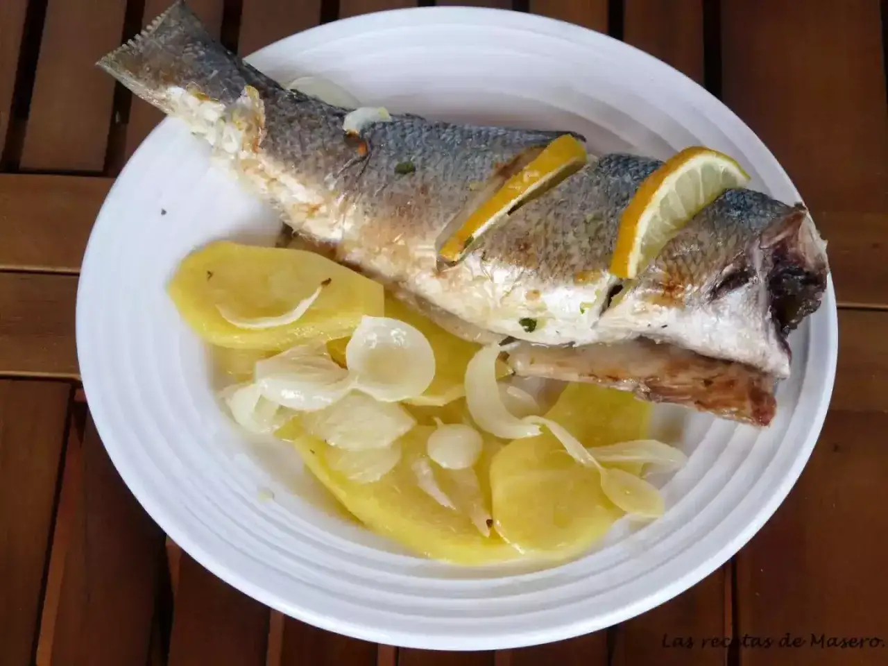 Lubina al horno con patatas y cebolla, decorada con rodajas de limón. Un plato sencillo y delicioso.