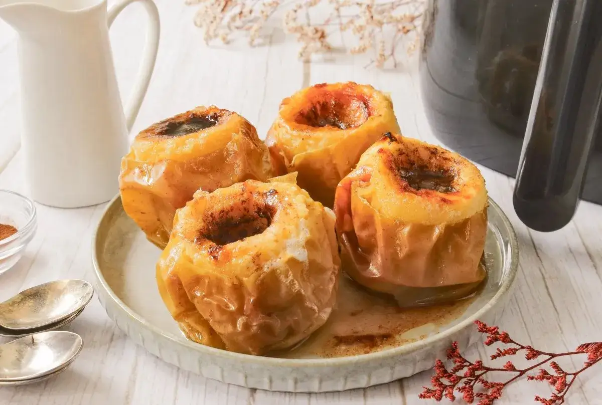 Cuatro manzanas asadas en freidora de aire, con el centro relleno de canela y azúcar, servidas en un plato.