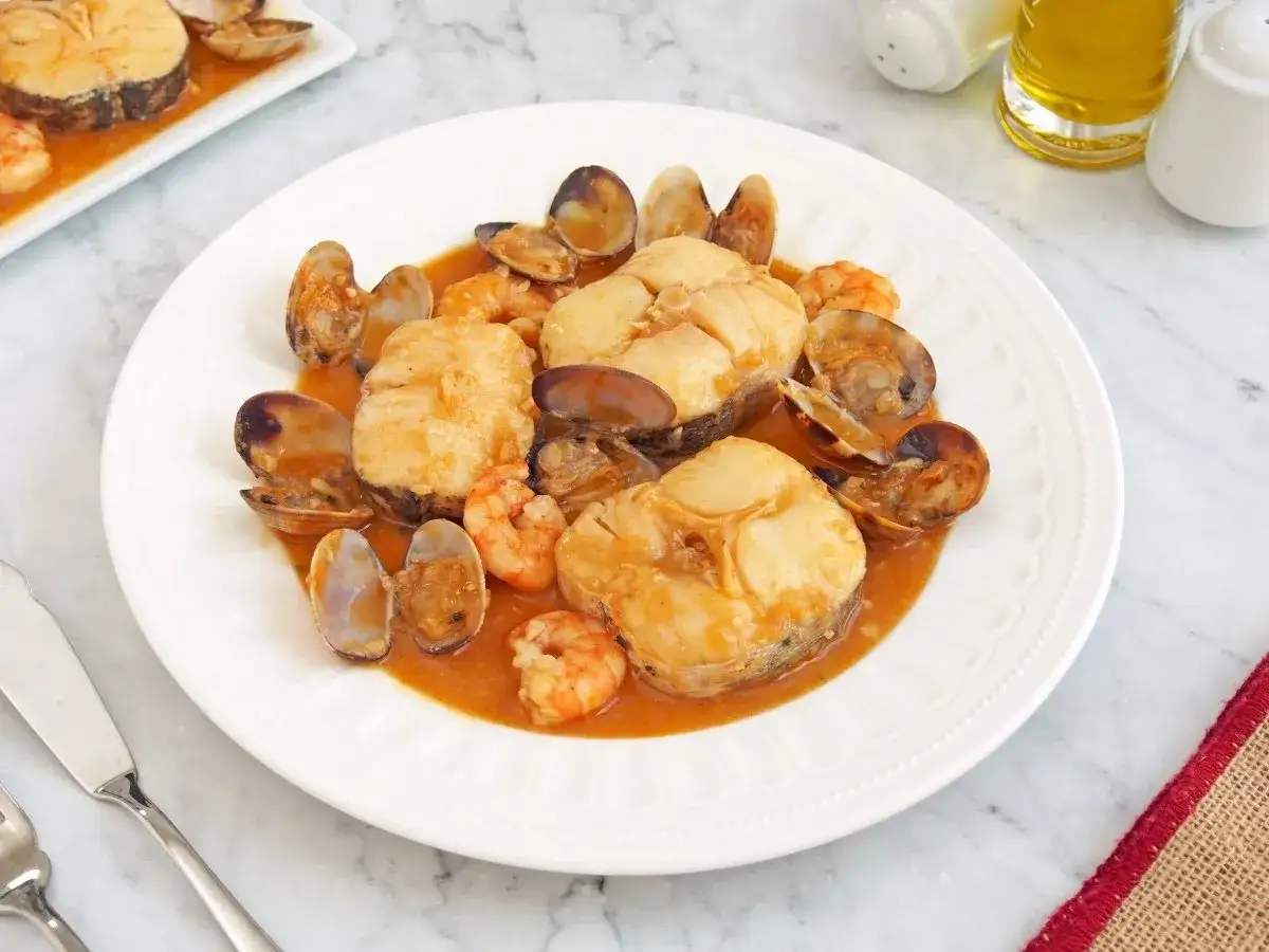 Merluza a la marinera con gambas y almejas en una salsa sabrosa.