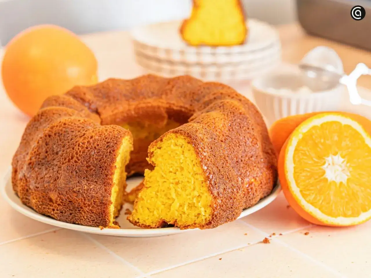 Un delicioso bizcocho de naranja, con una rebanada cortada, junto a naranjas frescas y un colador.