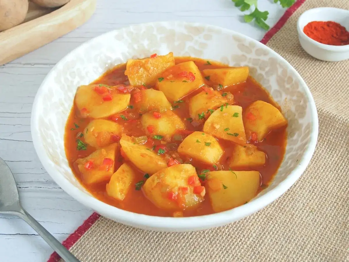 Patatas guisadas en salsa roja con pimientos y perejil. Un plato casero perfecto para cocer patatas y disfrutar.