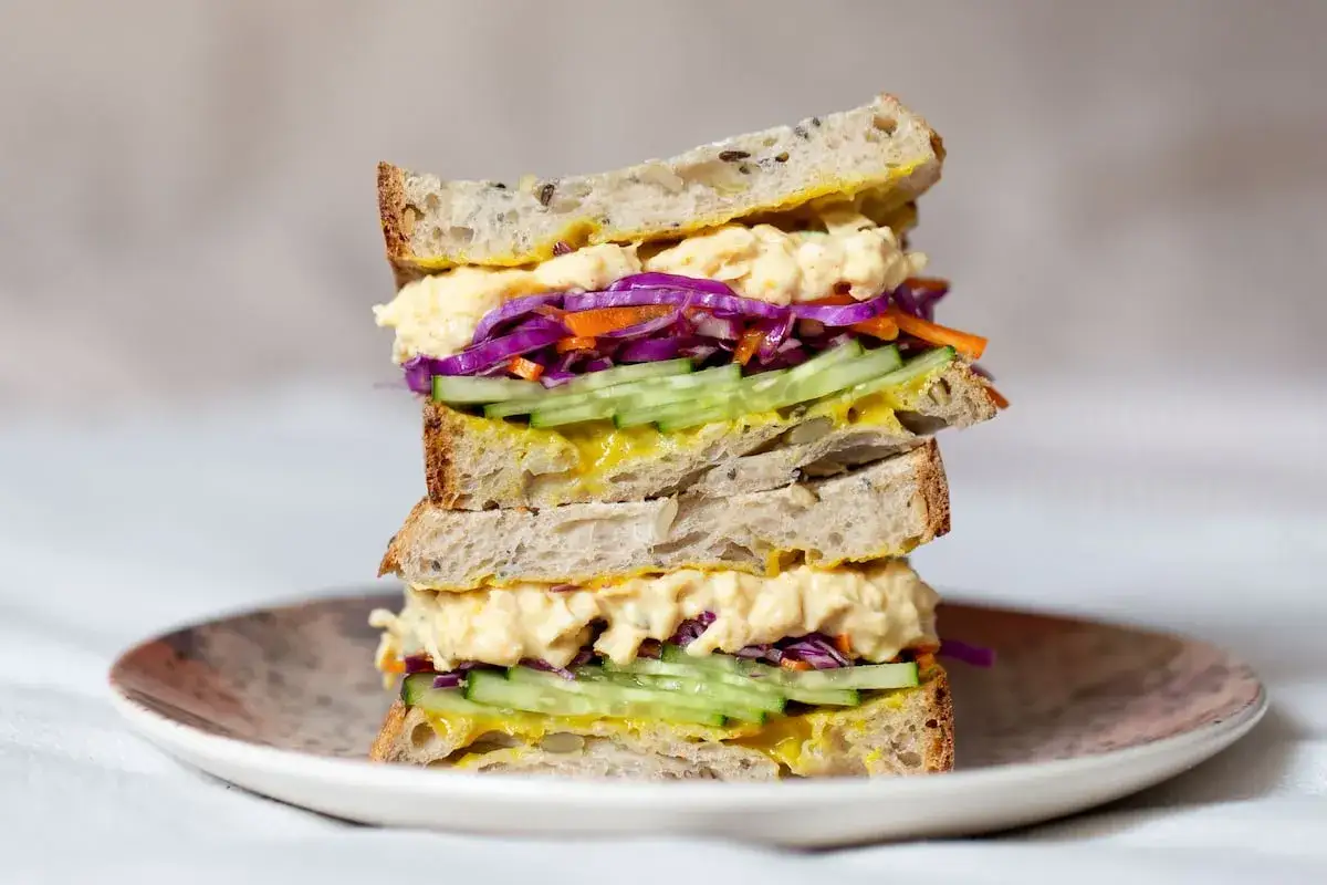 Un delicioso sandwich vegetal apilado, con pan r&uacute;stico, hummus cremoso, pepino, zanahoria y col morada.
