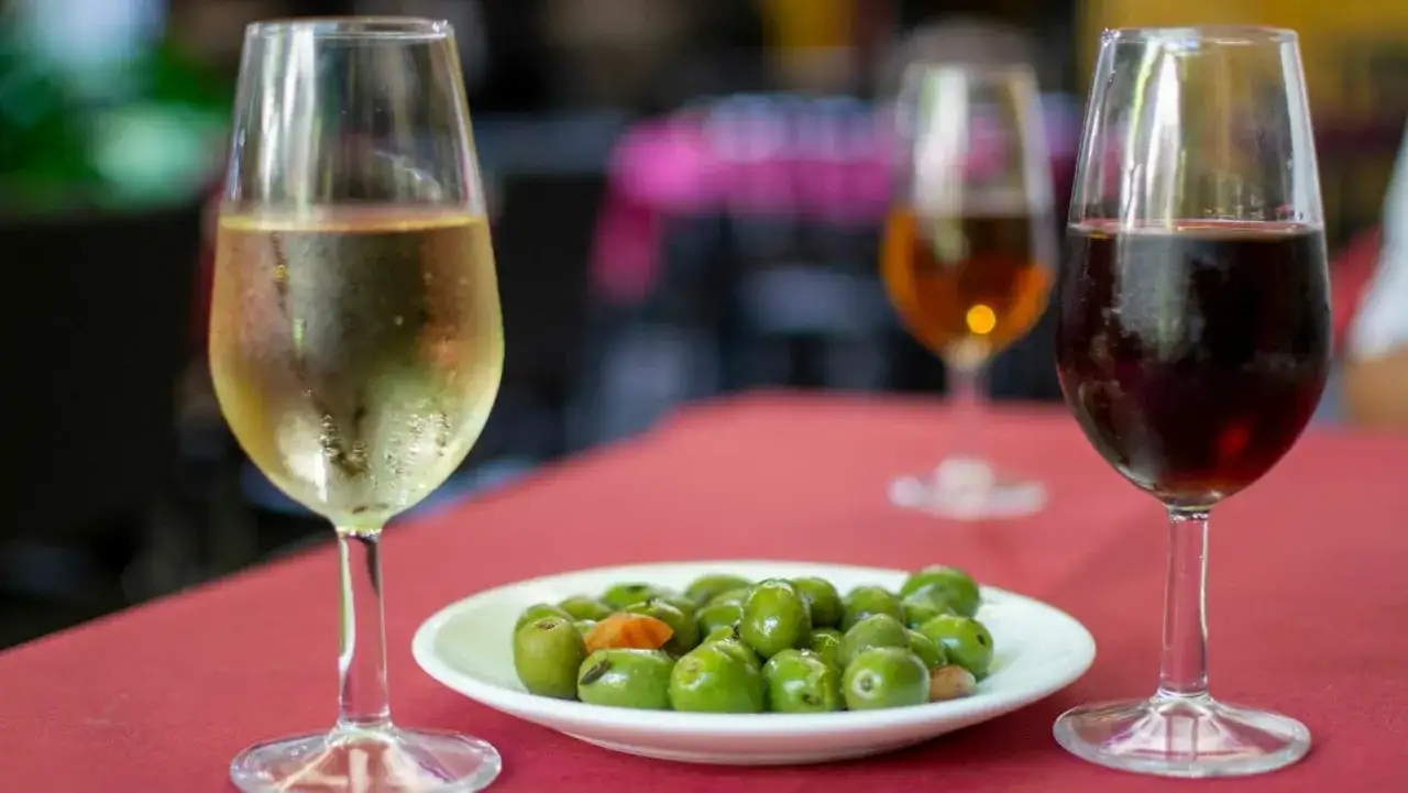Dos copas de jerez, una clara y otra oscura, junto a un plato de aceitunas verdes.