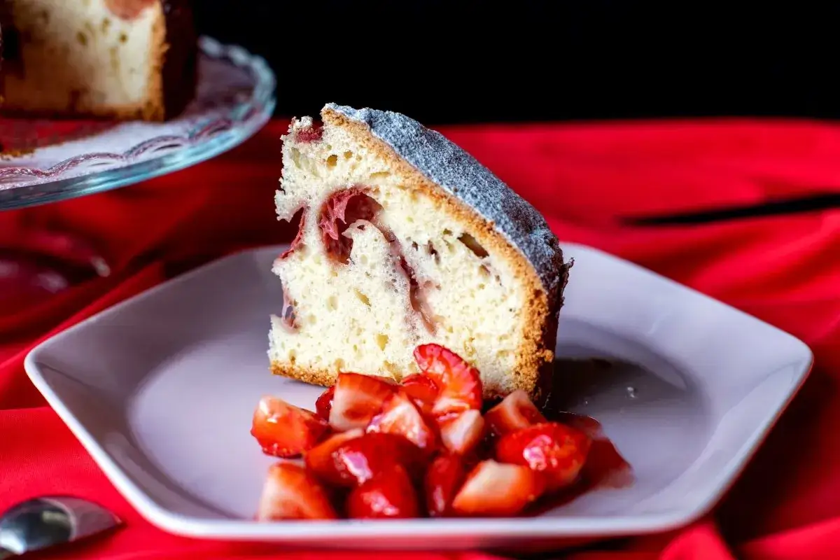 Rebanada de bizcocho de fresa esponjoso, con trozos de fresa en su interior y espolvoreado con az&uacute;car glas. Servido con fresas frescas picadas.