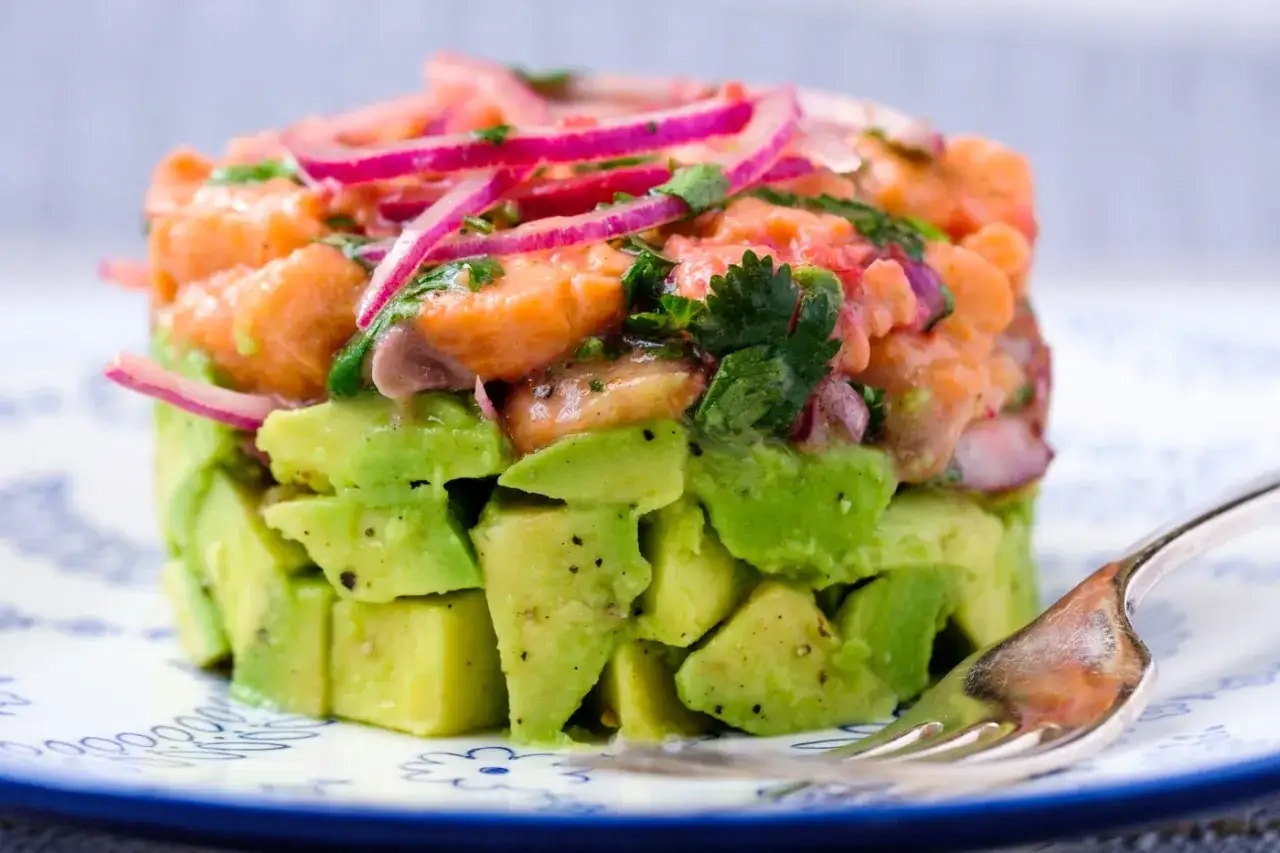 Delicioso tartar de salm&oacute;n y aguacate, con cebolla morada y cilantro fresco, servido en un plato blanco con borde azul.