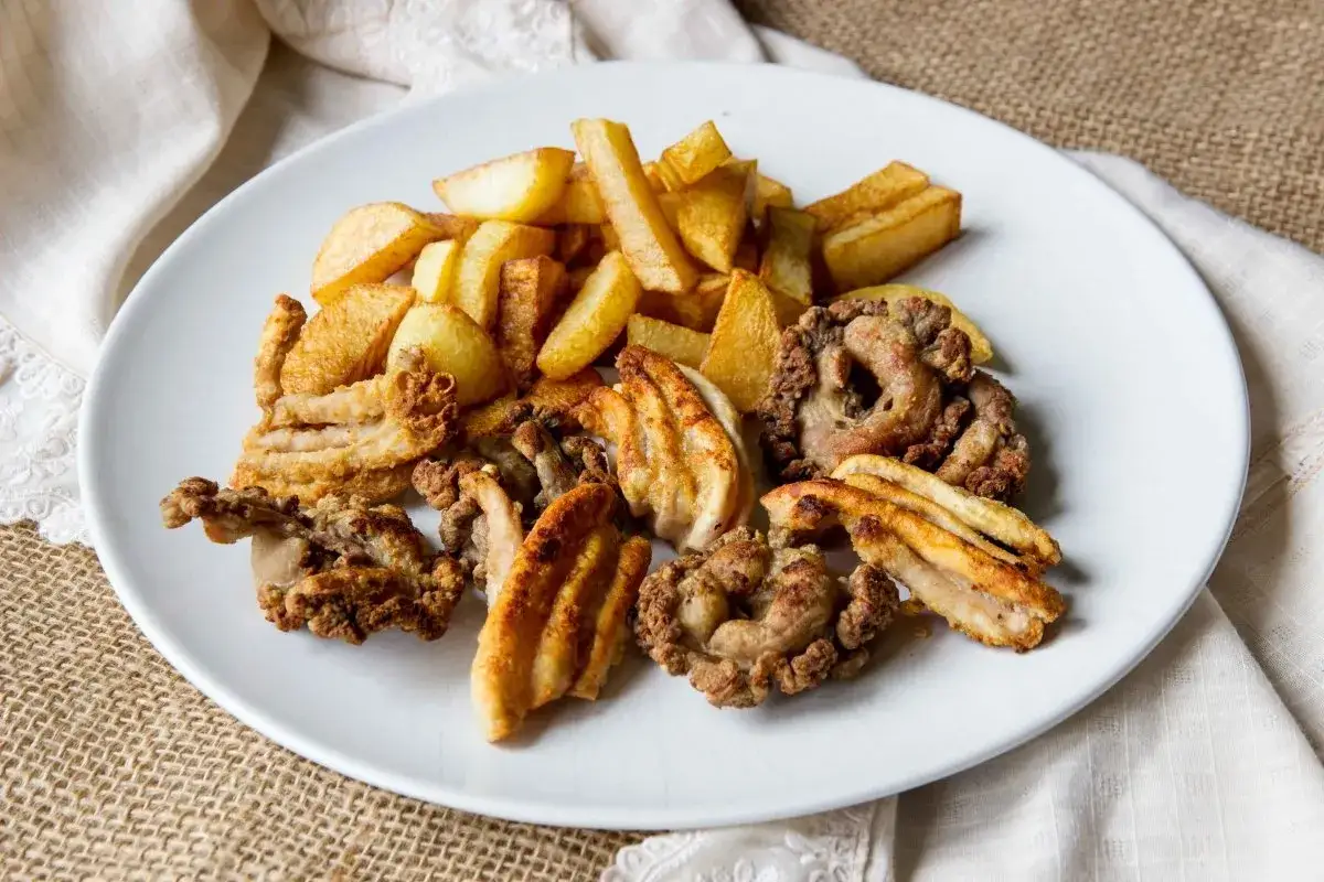 Plato de gallinejas y entresijos fritos, crujientes y dorados, acompa&ntilde;ados de patatas fritas caseras.